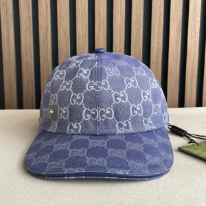 Blå keps från Gucci med GG-mönster - Snygg blå keps från Gucci i denim-look med ikoniskt GG-mönster över hela kepsen. Kepsen har böjd skärm och en liten guldfärgad GG-detalj på sidan. Perfekt för dig som vill sticka ut med en lyxig accessoar.