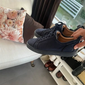 Christian Louboutins - Säljer ett par mörkblå sneakers från Christian Louboutin i mocka med den ikoniska röda sulan. Skorna har rund tå och platt sula, samt diskret broderad logga på sidan. Kommer med originalkartong, dustbag och äkthetsbevis.