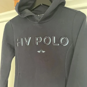 Mörkblå hoodie från HV Polo - Snygg mörkblå hoodie från HV Polo med stor logga broderad på bröstet och klassisk huva. Tröjan har långa ärmar och har ett mjukt material. Knappt använd så nyskick. Den är i stl M men skulle mer säga som en S.