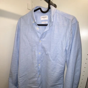 Babyblue skjorta från Lindbergh White - Klassisk Oxfordskjorta från Lindbergh White med fina detaljer som en diskret logga på vänster bröst. Skjortan är gjord av slitstarkt bomullstyg och är i färgen ljusblå, önskar ni andra färger så skriv till mig. Det finns en button-down krage och manschettens bredd kan justeras med två knappar. Den är gjord i superflex material.  Den är i slimfit passform, personligen tycker jag den passar bra som en overshirt. 