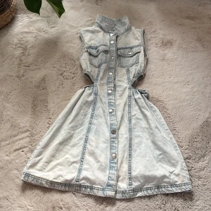 Ljus jeansklänning från Zara - Snygg ljusblå jeansklänning från Zara med ärmlös design, markerad midja och knappar hela vägen framtill. Två bröstfickor med lock. 