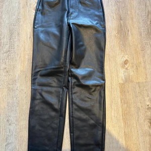 Svarta skinnbyxor från ONLY XS - Snygga svarta byxor i skinnimitation från ONLY. Modellen har raka ben, hög midja och bakfickor. Perfekta för dig som vill ha en edgy look med stilren vibe. Materialet är mjukt och följsamt syntetiskt skinn.
