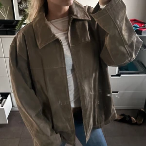 Oversized mockajacka från Machiavelli - Säljer en oversized mockajacka från Machiavelli i snyggt beige-brun ton. Jackan har klassisk krage, dragkedja framtill och breda ärmar. Perfekt för dig som gillar en chill och trendig look. Fodret är randigt i beige och vitt för extra stilpoäng.