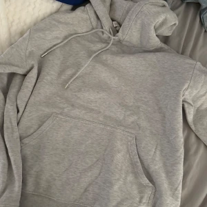 Ljusgrå hoodie XS med huva - En basic ljusgrå hoodie i storlek XS med huva och snörning. Tröjan har en stor magficka och är långärmad, perfekt för chill dagar. Tillverkad i mjuk bomullsmix som känns skön mot huden.