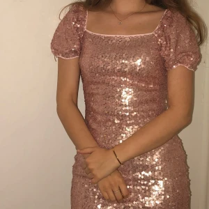 Rosa paljettklänning från Quiz - Superfin rosa kortklänning från Quiz med glittriga paljetter över hela klänningen. Puffärmar och fyrkantig urringning ger en trendig vibe. Klänningen har dragkedja i ryggen och är figurnära. Perfekt för dig som vill sticka ut!