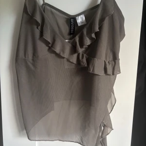 Brun/beige meshtopp - Supersöt beige linnetopp från Divided med tunna axelband och volangdetaljer längs urringningen. Den är i meshmaterial, har dock en liten fläck (se bild 2) 