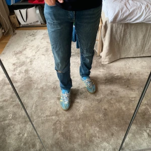 Blå jeans från Jack & Jones - Säljer ett par blå jeans från Jack & Jones med klassisk femficksdesign. Jeansen har slitningar och hål på benen samt en patchad bakficka. De är raka i modellen och har en snygg tvättad look som ger en avslappnad vibe.