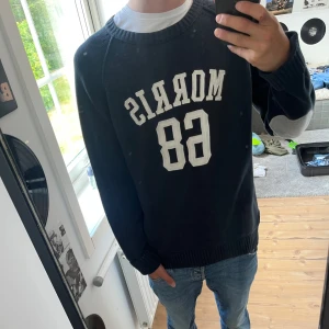 Morris svart stickad tröja med tryck - Säljer en mörkblå tröja från Morris med vit text och siffror på framsidan. Tröjan har långa ärmar och grå armbågslappar. Perfekt för till allt, storleken är large, den är förstor o för lång  på mig, är själv 172, priset kan diskuteras men kommer inte gå under 450