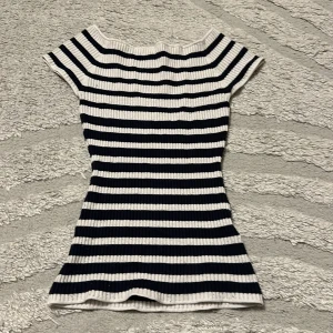 Randig ribbad topp i marinblått och vitt - Snygg ribbad topp med marinblå och vita horisontella ränder. Modellen är figurnära med korta ärmar och rundad halsringning. Perfekt för en fräsch och stilren look.