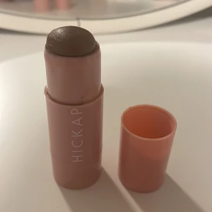 Hickap Hot Chocolate Bronzer Stick - Krämig bronzer och contour stick från Hickap i färgen Hot Chocolate. Kommer i en smidig rosa plastförpackning med vridfunktion. Perfekt för att skapa värme och definition i ansiktet med en djup brun nyans. Enkel att applicera direkt på huden och blenda ut.