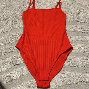 Röd ribbad boddy med smala axelband - Snygg röd boddy med smala axelband och ribbad struktur. Enkel och stilren design som ger en modern look.