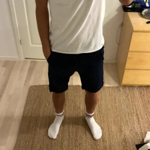 Mörkblå shorts från Jack & Jones - Snygga mörkblå shorts från Jack & Jones med klassisk passform och midwaist. Gjorda i mjuk bomull, perfekta för varma dagar. De har sidfickor, bälteshällor och stängs med knapp och dragkedja. Enkla att matcha med t-shirt eller skjorta.