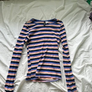 Randig långärmad tröja Divided XS - Säljer en ribbad långärmad tröja från H&M Divided i storlek XS. Tröjan har färgglada ränder i blått, svart, vitt, orange och rosa. Den är figurnära och har en klassisk rund halsringning. Perfekt för dig som gillar färg och mönster!