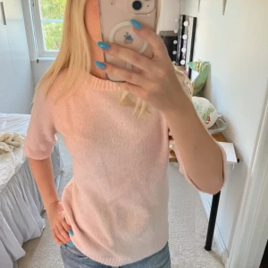 Ljusrosa stickad tröja med kort ärm - Superfin ljusrosa stickad tröja med korta ärmar och rund hals. Mjuk och skön, perfekt till våren eller svala sommarkvällar. Enkel och stilren design som är lätt att matcha med jeans eller kjol.