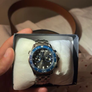 Omega Seamaster Diver 300M blå/silver - Säljer en Omega Seamaster Diver 300M med blå urtavla och silverfärgad länk i rostfritt stål. Klockan har vågmönstrad urtavla, kronograf och datumvisning. Boetten är rund och vridbar bezel i blått. Vattentät upp till 300 meter. Riktigt snygg och sportig design. Säljes billigt då jag behöver pengarna.