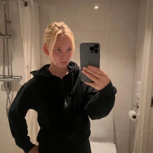 Svart hoodie med dragkedja - Svart hoodie med dragkedja framtill och huva. Modellen är loose fit och har långa ärmar. Perfekt för chill dagar eller när du vill ha något bekvämt och stilrent. Passar till allt och är enkel att matcha med andra plagg.