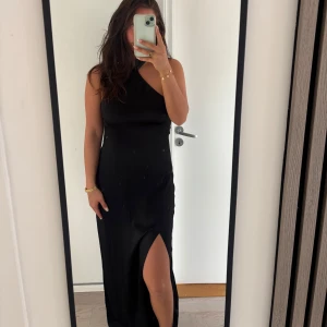 Svart långklänning med slits och oneshoulder - Säljer en elegant svart långklänning i satin med oneshoulder-design och hög slits framtill. Perfekt som balklänning. Nypris 850kr och skräddar sydd 600kr. Vi gjorde om den helt hos skräddaren och är då unik.