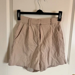 Beiga shorts från Amisu - Snygga beiga shorts från Amisu med hög midja och vida ben. Gjorda i ett lätt och luftigt material, perfekta för varma dagar. Klassisk design med hällor för bälte och fickor framtill.