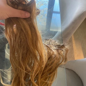 Löshår i mellanblond nyans - Säljer ett set löshår i mellanblond färg med inslag av varma toner. Löshåret är vågigt och har insydda clips för enkel applicering. Perfekt för att ge extra volym och längd till håret. Passar dig som vill ha en naturlig look.