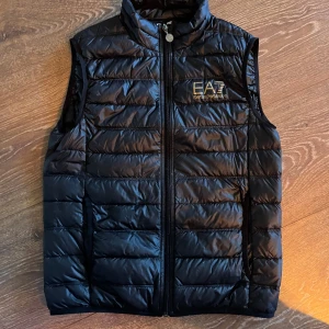 Svart dunväst från EA7 Emporio Armani - Säljer ju min EA7 väst då den har blivit för liten enligt mig den är knappt använd kanske max 10 gånger Den är i storlek S och väldigt bra skick Ny pris 1200kr säljer för endast 300kr