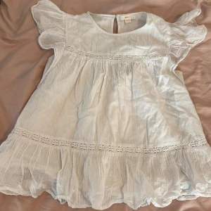 Ljusvit volangblus från Gina Tricot - Supersöt ljusvit Blus från Gina Tricot med volangdetaljer och spets längs midjan och nederkanten. Den har korta puffärmar och är tillverkad i ett tunt, luftigt material som passar perfekt till varma dagar.