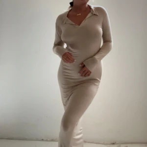 Beige långklänning med krage - Säljer en beige långklänning med lång ärm och v-ringning samt klassisk krage. Klänningen har en tight passform och är tillverkad i ett mjukt, stretchigt material som sitter snyggt på kroppen. Storlek 40 men sitter som en s/m 