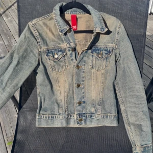 Klassisk jeansjacka - Säljer en klassisk blå jeansjacka med knappar framtill och två bröstfickor. Jackan har en tidlös design med krage och långa ärmar. Perfekt att slänga över en t-shirt för en avslappnad look.