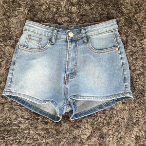 Lågmidjade Ljusblå jeansshorts  - Snygga ljusblå jeansshorts med  stora fickor med mycket plats och lågmidjade. Shortsen har synliga sömmar och knapp- samt dragkedjestängning framtill. Perfekta för varma dagar och enkel att matcha med olika toppar.