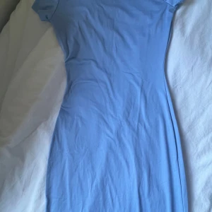 Ljusblå tight långklänning - Säljer en enkel och stilren ljusblå långklänning med korta ärmar. Klänningen har en tight passform och är tillverkad i ett mjukt och stretchigt material, perfekt för en avslappnad men snygg look.