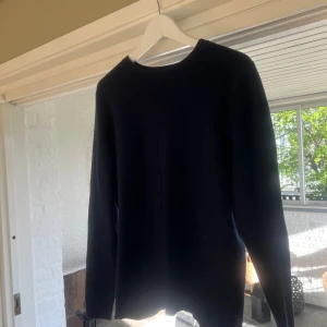 Mörkblå stickad tröja - En enkel och stilren mörkblå stickad tröja med rund halsringning. Tröjan har långa ärmar och ribbade muddar vid hals. Storlek S
