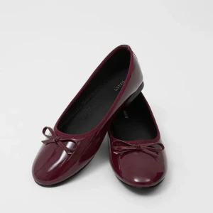 Vinröda ballerinaskor med rosett - Snygga vinröda ballerinaskor i glansigt material med en söt rosett framtill. Skorna har rund tå och platt sula, perfekta för en stilren och klassisk look.