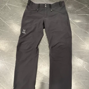  Haglöfs byxor - Svarta friluftsbyxor från Haglöfs med diskret logga på låret. Byxorna har normal passform, dragkedja och knappar i midjan samt praktiska fickor. Perfekta för utomhusaktiviteter och äventyr.