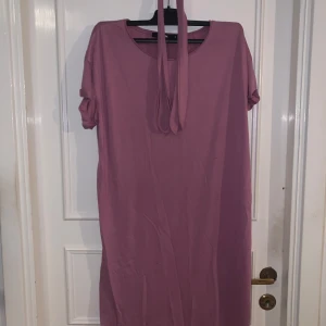 Rosa klänning med knytband från BikBok - En enkel och stilren rosa klänning från BikBok med korta ärmar och knytband i halsen. Klänningen har rak passform och är tillverkad i ett mjukt material som känns skönt mot huden. Perfekt för en avslappnad look.