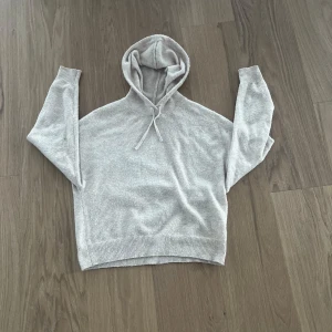 Beige kashmir  - Kashmir med huva och dragsko. Tröjan har långa ärmar och ribbade muddar vid ärmslut och nederkant. Perfekt för en avslappnad stil.