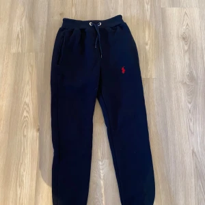 Maurinblåa  mjukisbyxor från Polo Ralph Lauren - Svarta mjukisbyxor från Polo Ralph Lauren med dragsko i midjan och två sidofickor. Byxorna har en liten röd broderad logga på vänster sida och är tillverkade i mjukt material. Perfekta för en avslappnad stil.