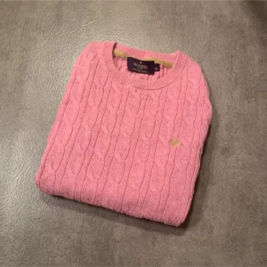 Rosa kabelstickad tröja från Morris Lady - Säljer en rosa kabelstickad tröja från Morris Lady i 100% pima bomull. Tröjan har rund halsringning, lång ärm och en liten broderad logga på bröstet. Perfekt för dig som gillar klassisk och stilren design. Tröjan är i bra skick men tagen vid nacken är av på ett ställe, visas i bild 4. Bara att höra av sig vif funderingar!