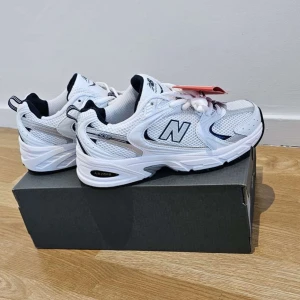 Vita sneakers från New Balance - Säljer ett par fräscha vita New Balance sneakers med svarta och grå detaljer. Skorna har klassisk mesh och syntetmaterial, rund tå och snörning. Perfekta för en sportig och stilren look.