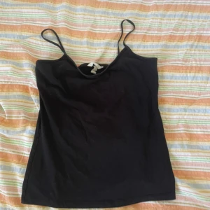 Svart linnetopp från H&M - En enkel svart linnetopp från H&M Basics med tunna axelband. Perfekt att matcha med jeans eller kjol för en stilren look. Gjord i mjuk bomull för extra komfort.