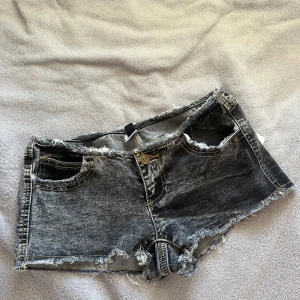 ”No waist” Svarta lågmidjade jeansshorts med fransar från usa - Säljer ett par svarta jeansshorts från JNK med slitna detaljer och fransig kant. Shortsen har klassisk femficksdesign, låg midja och råa benslut för en edgy look. Perfekta för varma dagar och festivaler. Står strl M/L men stämmer ej, storlek xs/s!!