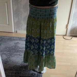 Mönstrad långkjol från Zara - Säljer en långkjol från Zara, Kjolen har ett färgstarkt mönster i blått, grönt och gult samt volang nertill. Kjolen är 90 cm lång. Och resår i midjan. 