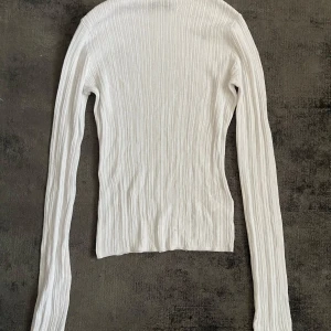 Vit ribbad långärmad topp - Säljer en vit långärmad topp med ribbad struktur. Tröjan är figurnära och har en enkel, stilren design som passar till mycket. Perfekt att styla med jeans eller kjol för en clean look. Genomskinlig 