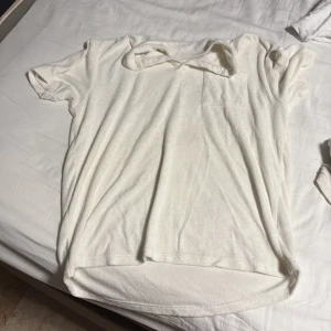 Vit t-shirt med bröstficka - Säljer en enkel vit t-shirt med kort ärm och liten bröstficka. T-shirten har rund halsringning och är i mjukt material, perfekt för vardagslooken.