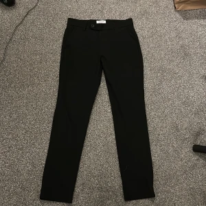 Svarta kostymbyxor ifrån Jack&Jones - Snygga svarta kostymbyxor med normal passform och raka ben. Byxorna har diskreta fickor fram och bak samt stängs med knapp och dragkedja. Perfekta till en stilren look.