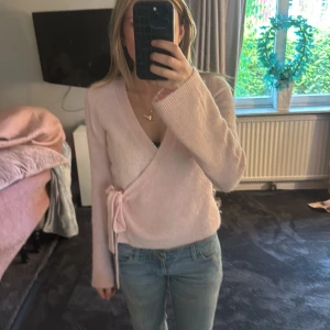 Ljusrosa omlottkofta med knytband - Säljer en supermjuk ljusrosa omlottkofta med knytband i sidan. Tröjan har lång ärm och är perfekt att styla med jeans eller kjol. Enkel och stilren design som passar till många tillfällen.