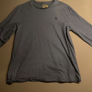 Oanvänd Blå långärmad tröja från Polo Ralph Lauren - Säljer en oanvänd blå långärmad tröja från Polo Ralph Lauren med klassisk rund hals och diskret logga broderad på bröstet. Tröjan är i bomull och har en slim fit passform. Perfekt för en stilren och enkel look.