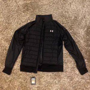 Svart pufferjacka från Under Armour - Säljer en svart pufferjacka hybridjacket ifrån Under Armour. Storleken är M och den är helt oanvänd med prislappen kvar. Glömde lämna tillbaka på öppet köp så säljer den för mycket billigare här. Snygg till sommarkvällar och lite blåsigare dagar. Vid intresse skriv. Pris kan diskuteras 