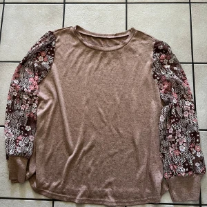 Beige tröja med blommiga ärmar - Säljer en beige tröja med långa ärmar i blommigt mönster i rosa, vitt och brunt. Tröjan har rund halsringning och muddar vid ärmsluten. Perfekt för dig som vill ha något unikt och bekvämt.
