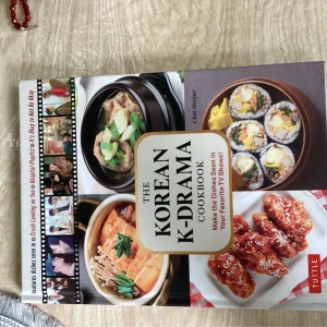 The Korean K-Drama Cookbook - En kokbok med koreanska rätter inspirerade av populära K-dramas. Omslaget visar bilder på traditionella maträtter som soppa, kimbap och friterad kyckling. Perfekt för dig som vill laga maten du sett i dina favoritserier.