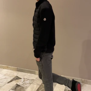 Svart moncler cardigan  - Säljer en svart pufferjacka från Moncler med diskret logga på ärmen. Jackan har lång ärm, hög krage och dragkedja framtill. Perfekt för kyligare dagar och ger en stilren look. Kan ge ner i pris vid snabb affär! 