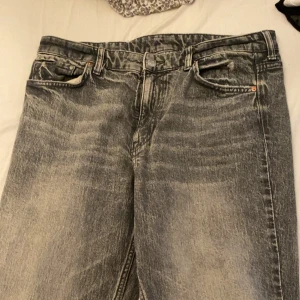 Grå tvättade jeans med raka ben - Säljer ett par grå tvättade jeans med raka ben och klassisk femficksdesign. Jeansen har normal passform och hög midja, med slitningar och en vintagekänsla i tvätten. Perfekta för en avslappnad stil.